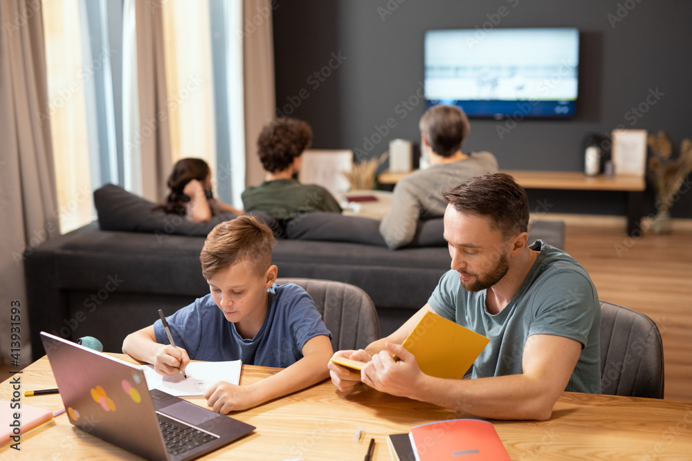 Young man with open book reading text while sitting next to his cute little son Young man with open book reading text while sitting next to his cute little son