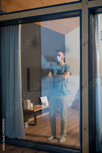 Young contemporary man in casualwear and protective mask standing by window