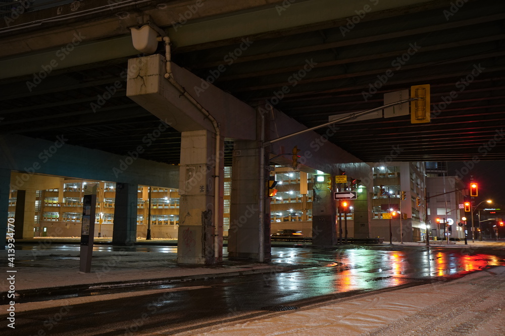 Urban city bridge underpass at night time during rainy day with reflection on the streets and big intersection