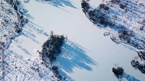 Aerial revealing birdseye view of snowy bog landscape with frozen lakes in sunny winter day, Dunika peat bog (Rucava, Latvia), wide angle drone shot camera tilt up photo