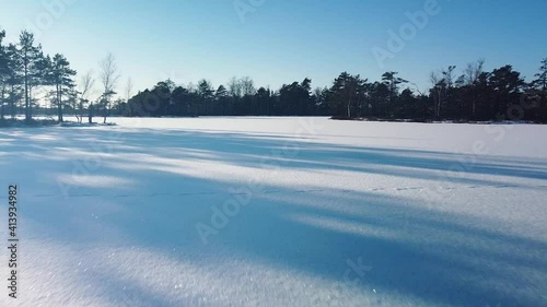 Aerial view of snowy bog landscape with frozen lakes in sunny winter day, Dunika peat bog (Rucava, Latvia), wide angle drone shot moving forward low to the ground photo