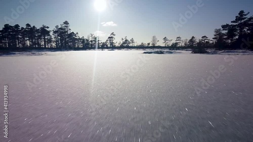 Aerial view of snowy bog landscape with frozen lakes in sunny winter day, Dunika peat bog (Rucava, Latvia), wide angle ascending drone shot moving forward fast photo