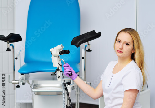 young attractive female gynecologist holding a colposcope or microscope against the background of a gynecological chair in a modern clinic. Women s health.
