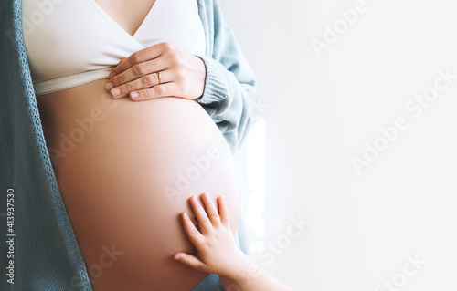 Concept of Family, Pregnancy, Motherhood, New Life. Close-up beautiful pregnant woman belly with her hand and little child hand. Expectant mother and kids waiting for baby birth. photo