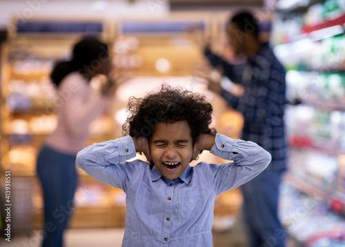 Little black girl covering her ears and shouting while her parents arguing at supermarket