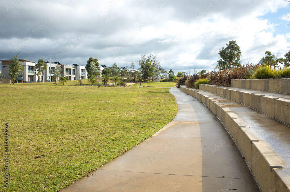 A concrete pedestrian footpath in a park with some modern residential houses or  homes in the distance. A public suburban park in an Australian neighbourhood.