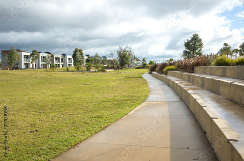 A concrete pedestrian footpath in a park with some modern residential houses or homes in the distance. A public suburban park in an Australian neighbourhood.