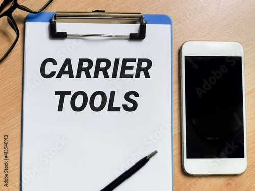 Business and technology concept. Phrase CARRIER TOOLS written on paper clipboard with pen,smartphone and eye glasses. 