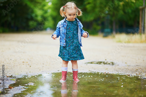 Child wearing red rain boots and jumping in puddle on a summer day © Ekaterina Pokrovsky