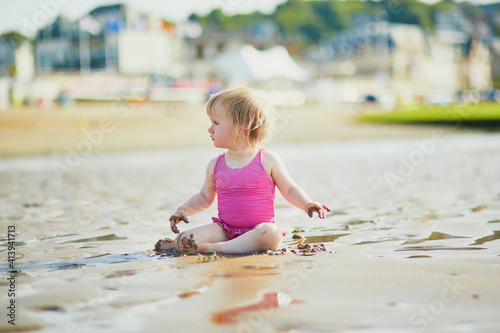 Adorable toddler girl playing with sand on the beach. Child spending vacation on the Atlantic coast in Normandy, France. Outdoor activities for kids