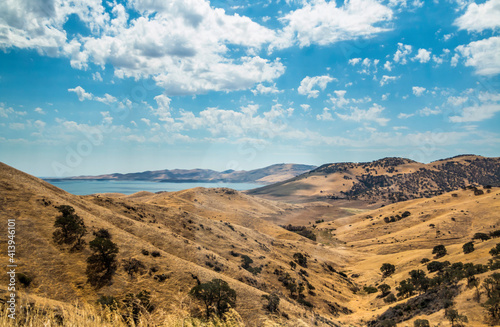 calm lake under a blue sky with cotton like clouds above the sky and surrounded by desert like terrain in Central Valley California.