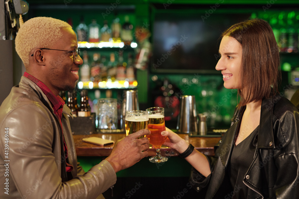 Happy young African man and his girlfriend clinking with glasses of beer in bar Happy young African man and his girlfriend clinking with glasses of beer in bar
