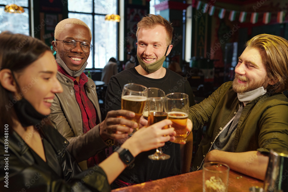Group of young football fans clinking with glasses of beer over bar counter