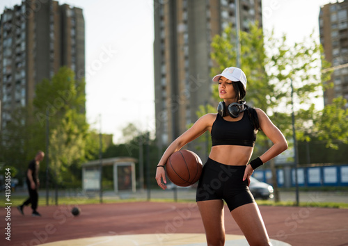 Attractive young woman in short shorts posing with ball on basketball court 