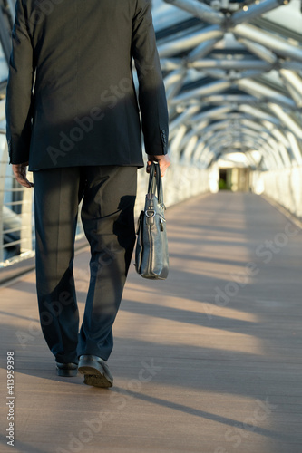 Rear view of delegate or businessman carrying handbag while moving along aisle