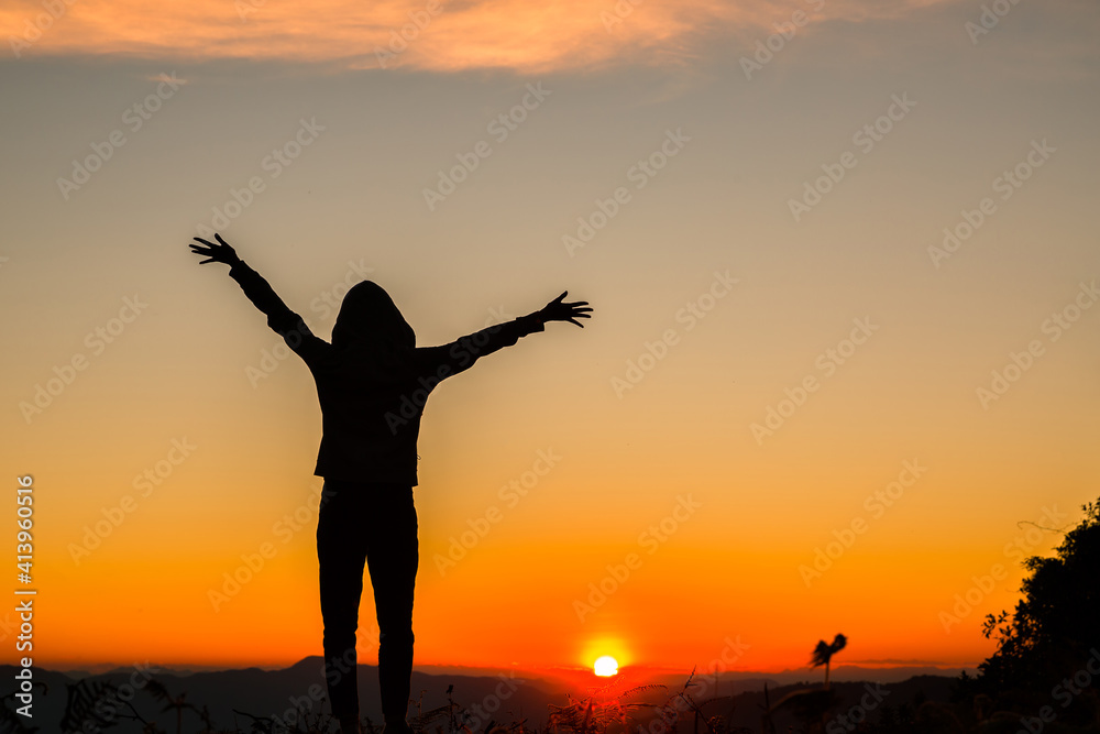 Silhouette of a woman with hands raised in the sunset