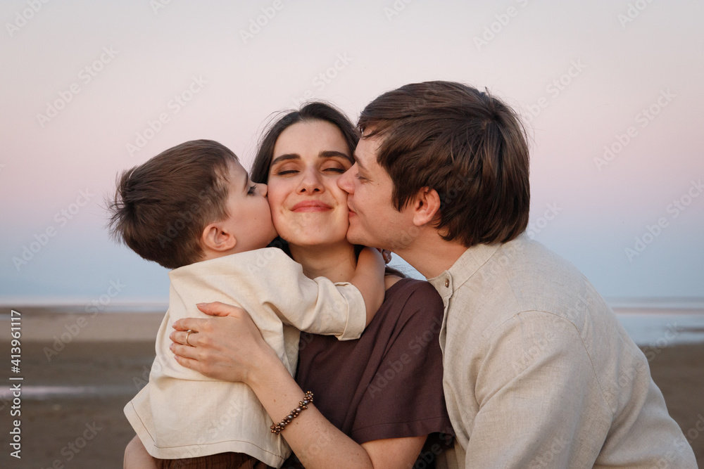 Young father with his little son kissing his wife and mother. Family look linen clothes.
