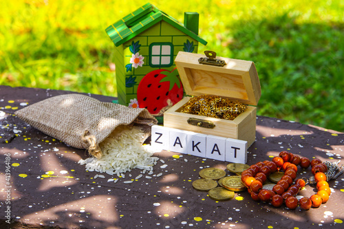 ZAKAT word coin stacked, rice grain in bowl and mini house on nature background. Muslim concept for zakat property, income and 