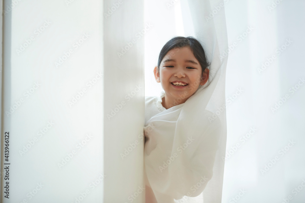 Happy little girl opening window curtains at home Happy little girl opening window curtains at home