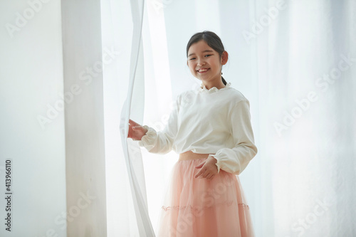 Happy little girl opening window curtains at home