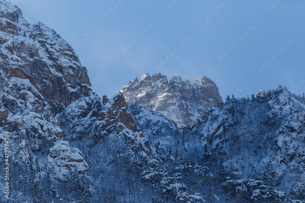 Picturesque snow-capped rocks against the blue sky. The inaccessible mountains are covered in snow during a severe blizzard. Rock climbing.
