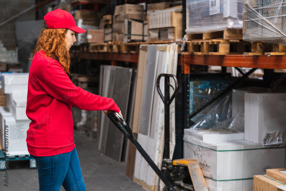Female worker using a pallet jack at a warehouse dressed in red