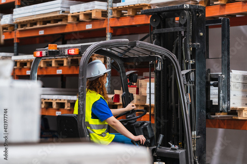 View from behind industrial female worker wearing a medical mask using a forklift in a warehouse