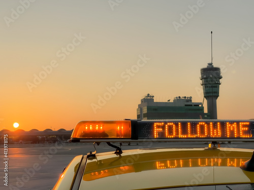 Bild auf Leinwand "follow me" light bar on airfield vehicle with sunset control tower background