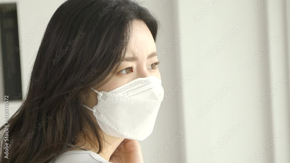 Young beautiful woman in a medical mask stands by the window Young beautiful woman in a medical mask stands by the window