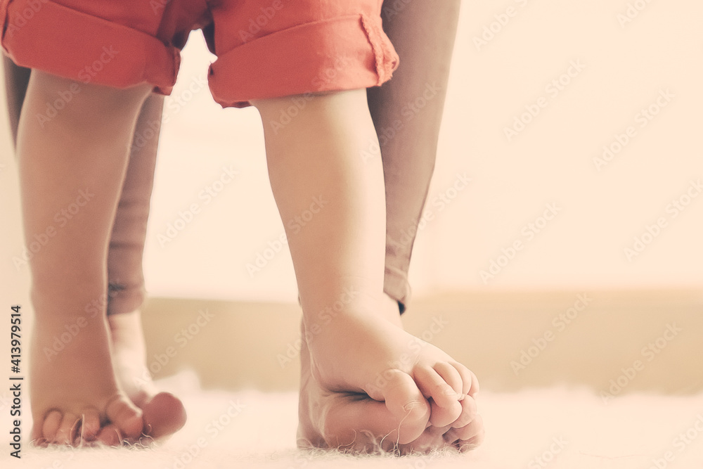 Sweet legs of baby standing on moms feet. Kid learning to walk with moms support. Cropped shot. Parenthood and childhood concept Sweet legs of baby standing on moms feet. Kid learning to walk with moms support. Cropped shot. Parenthood and childhood concept