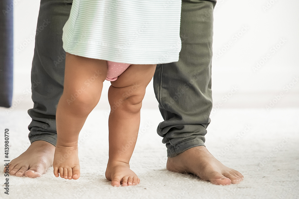 Barefooted legs of baby trying to walk in front of mom. Kid making first steps with moms support. Cropped shot. Parenthood and childhood concept Barefooted legs of baby trying to walk in front of mom. Kid making first steps with moms support. Cropped shot. Parenthood and childhood concept
