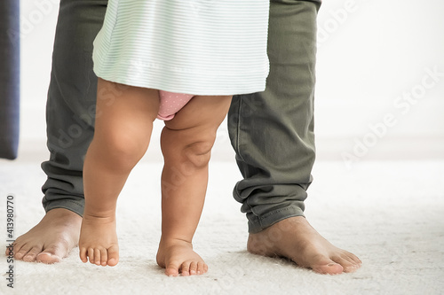 Barefooted legs of baby trying to walk in front of mom. Kid making first steps with moms support. Cropped shot. Parenthood and childhood concept