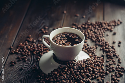 a cup of hot coffee on a wooden table and sprinkled beans close-up