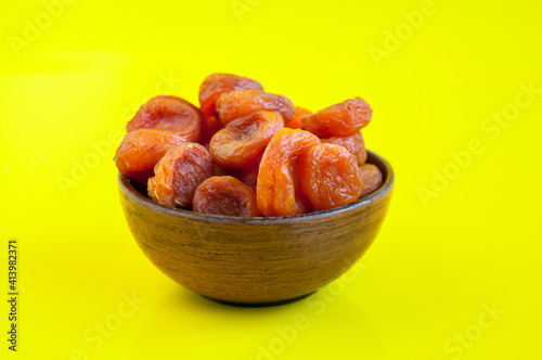 Dried fruits of orange dried apricots in a clay cup on a yellow background