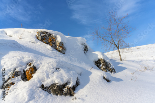 At the top of the mountain in winter. Rocky snowy landscape with a tree against a blue sky with white clouds on a very frosty winter day. Winter nature in all its glory and bright colors. Ural (Russia