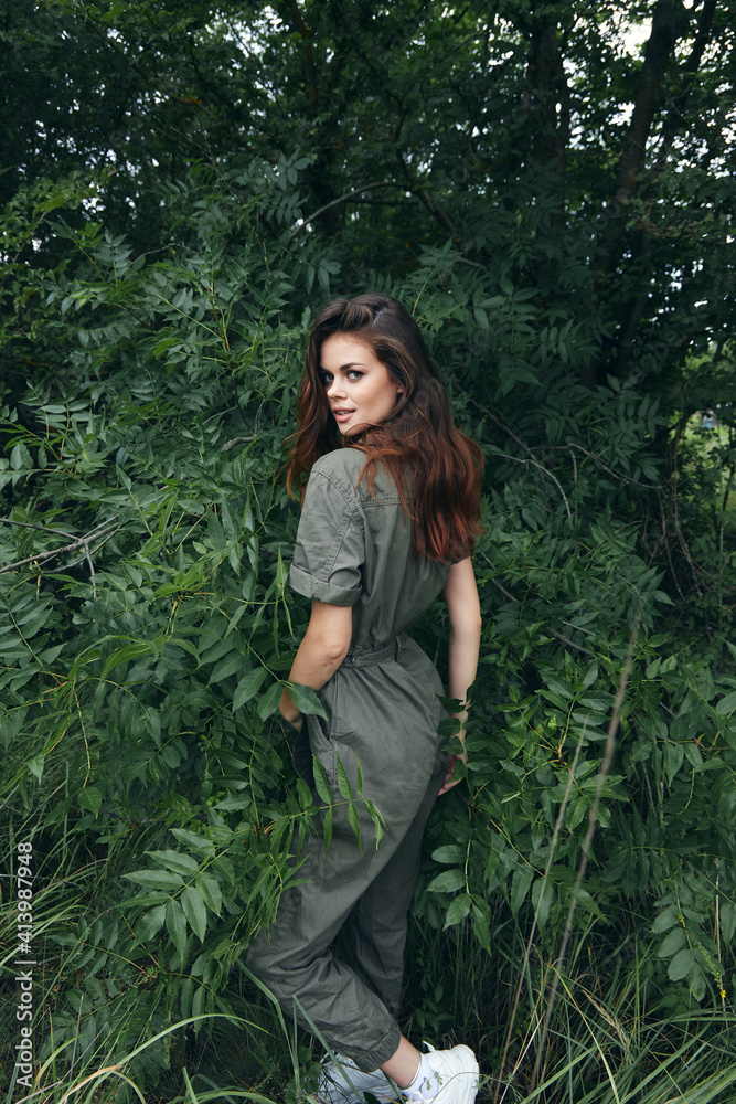 Woman In a trendy jumpsuit near green bushes and white sneakers outdoors green leaves Woman In a trendy jumpsuit near green bushes and white sneakers outdoors green leaves