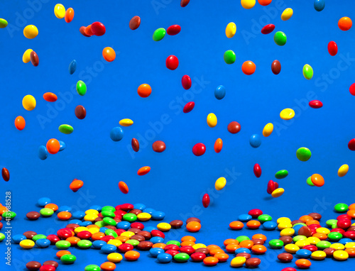 Rainbow Colored Candy Coated Chocolate Buttons Falling into a Pile on a Blue Background