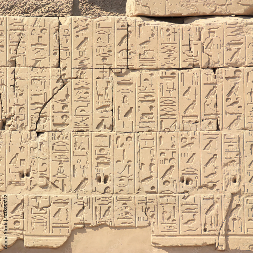 A wall with lots of hieroglyphs in the temple of Karnak in Egypt. The close-up shows the many symbols and characters of ancient Egyptian culture. The wall is illuminated by the sun.
