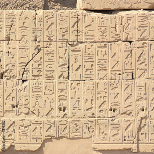 A wall with lots of hieroglyphs in the temple of Karnak in Egypt. The close-up shows the many symbols and characters of ancient Egyptian culture. The wall is illuminated by the sun.