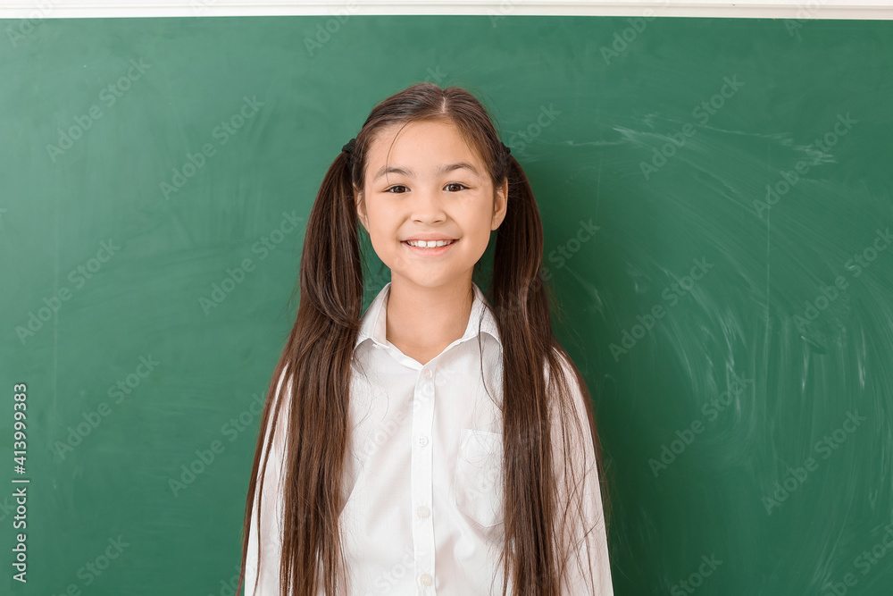 Little schoolgirl near chalkboard in classroom