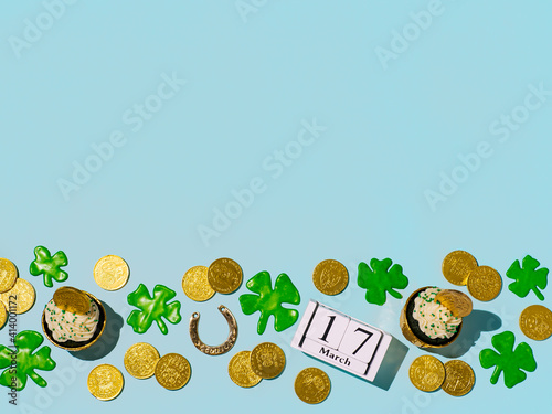 St Patrick's Day concept with copy space. Modern still life with lucky symbols and sweet food for Saint Patrick's Day party. Green velvet cupckake, shamrock, golden coins, horseshoe on blue background photo