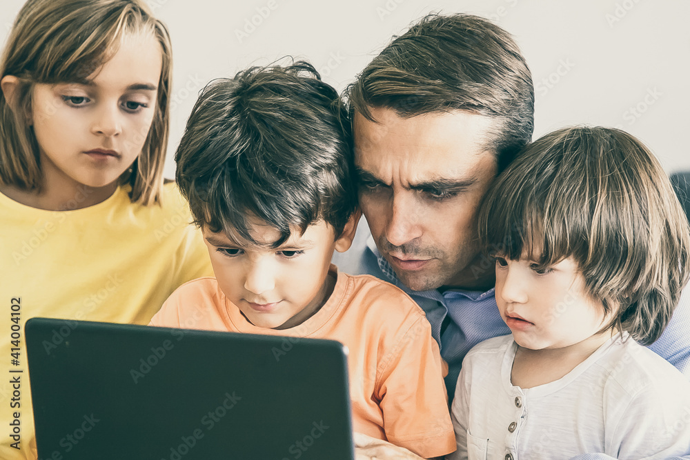 Concentrated father and serious kids looking at screen. Caucasian middle-aged dad typing on laptop screen and children watching his work. Fatherhood, childhood and digital technology concept Concentrated father and serious kids looking at screen. Caucasian middle-aged dad typing on laptop screen and children watching his work. Fatherhood, childhood and digital technology concept