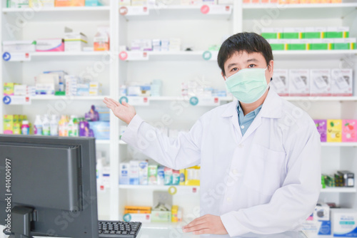 Asian professional young pharmacist wearing face mask while standing at drugstore.