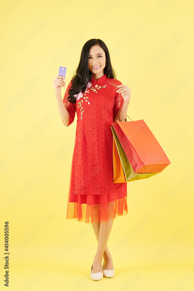 Portrait of pretty young Asian woman holding shopping bags and credit card and smiling at camera