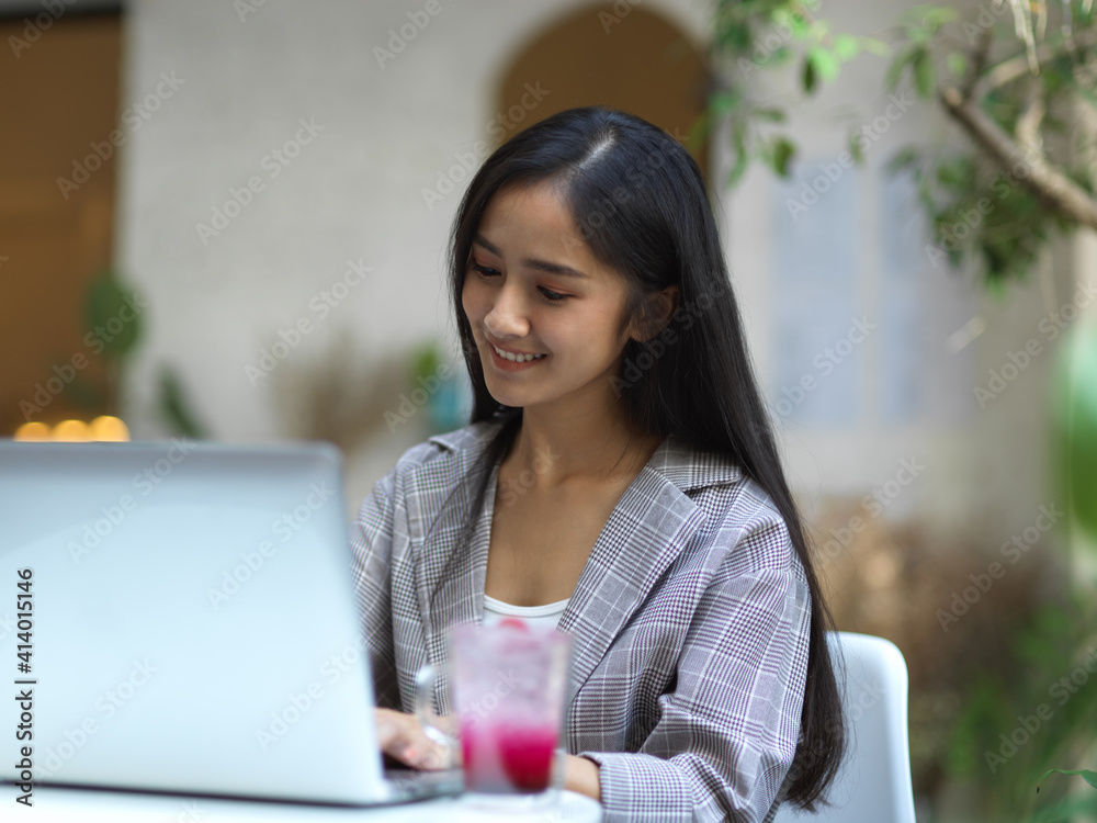 Smiling businesswoman working with laptop on coffee table in garden of the front of cafe Smiling businesswoman working with laptop on coffee table in garden of the front of cafe