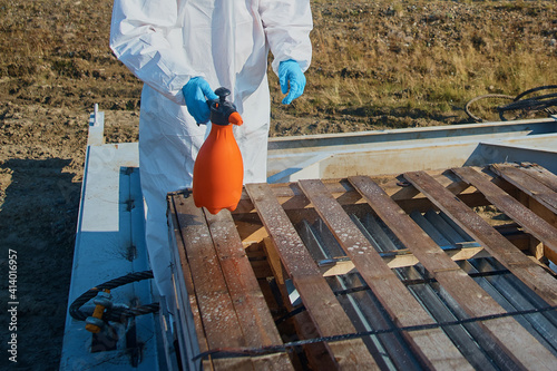 A worker in a suit, gloves, mask with equipment disinfects the surface in the warehouse. Sanitary treatment of the surface of a wooden box in the warehouse. Close-up.