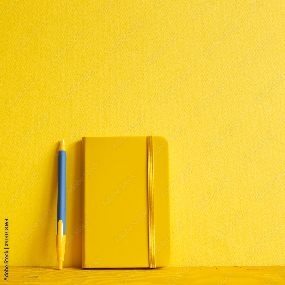 Yellow notebook and pen on wooden table. yellow background