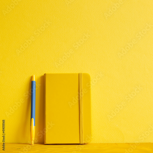 Obraz na płótnie Yellow notebook and pen on wooden table. yellow background w salonie