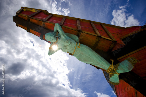 A Statue of a Mermaid Tied Up to the Bow of a Ship with Blue Sky and Clouds in the Background
