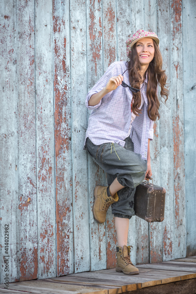 Beautiful woman with long jair and sunglasses, wear denim clothes, jeans with suitcase over wooden grunge, vintage background